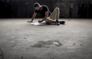Man sat on ground writing at an agle